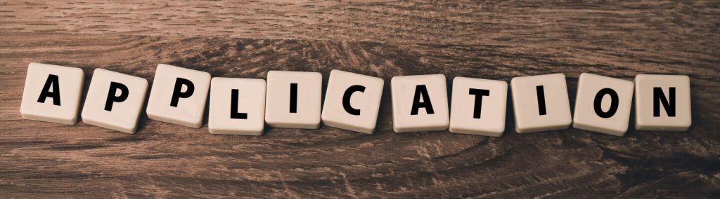 Scrabble tiles spelling out the word application, displayed on a wooden table.