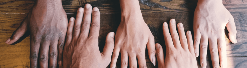 Multiple hands laying flat on a wooden table.