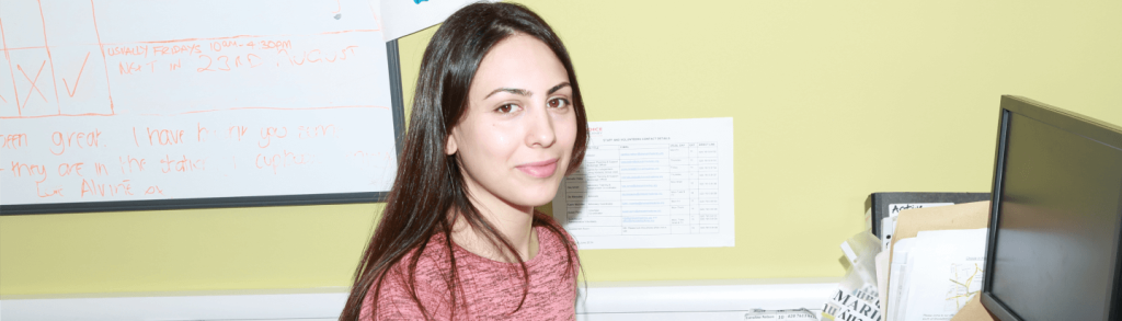 A girl looking at the camera while seated in an office setting, with a computer in front of her.