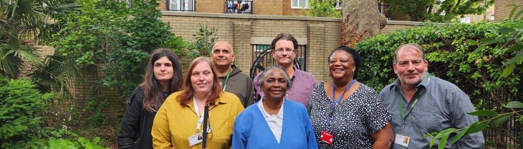 The choice in hackney staff members, smiling and standing together in a lush, green, leafy area.