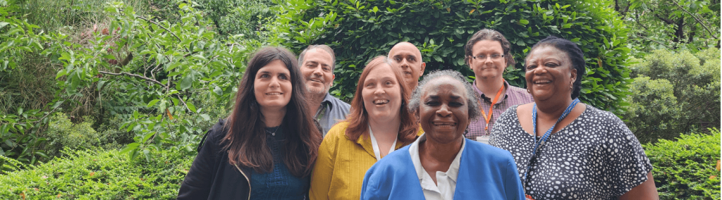 The choice in hackney staff members, smiling and standing together in a lush, green, leafy area.